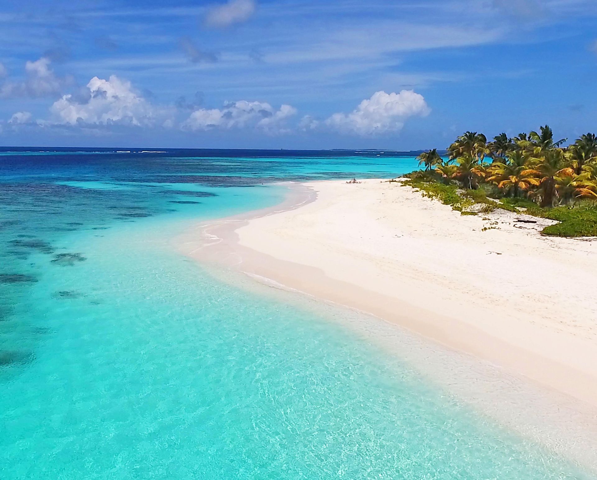 White sand beach, turquoise water, and palm trees under a blue sky with clouds.