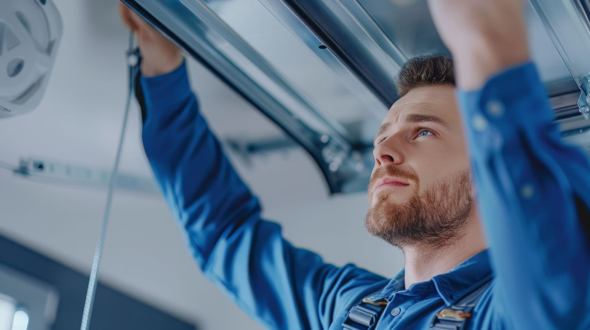 Person in blue workwear adjusting equipment on an overhead garage door system.