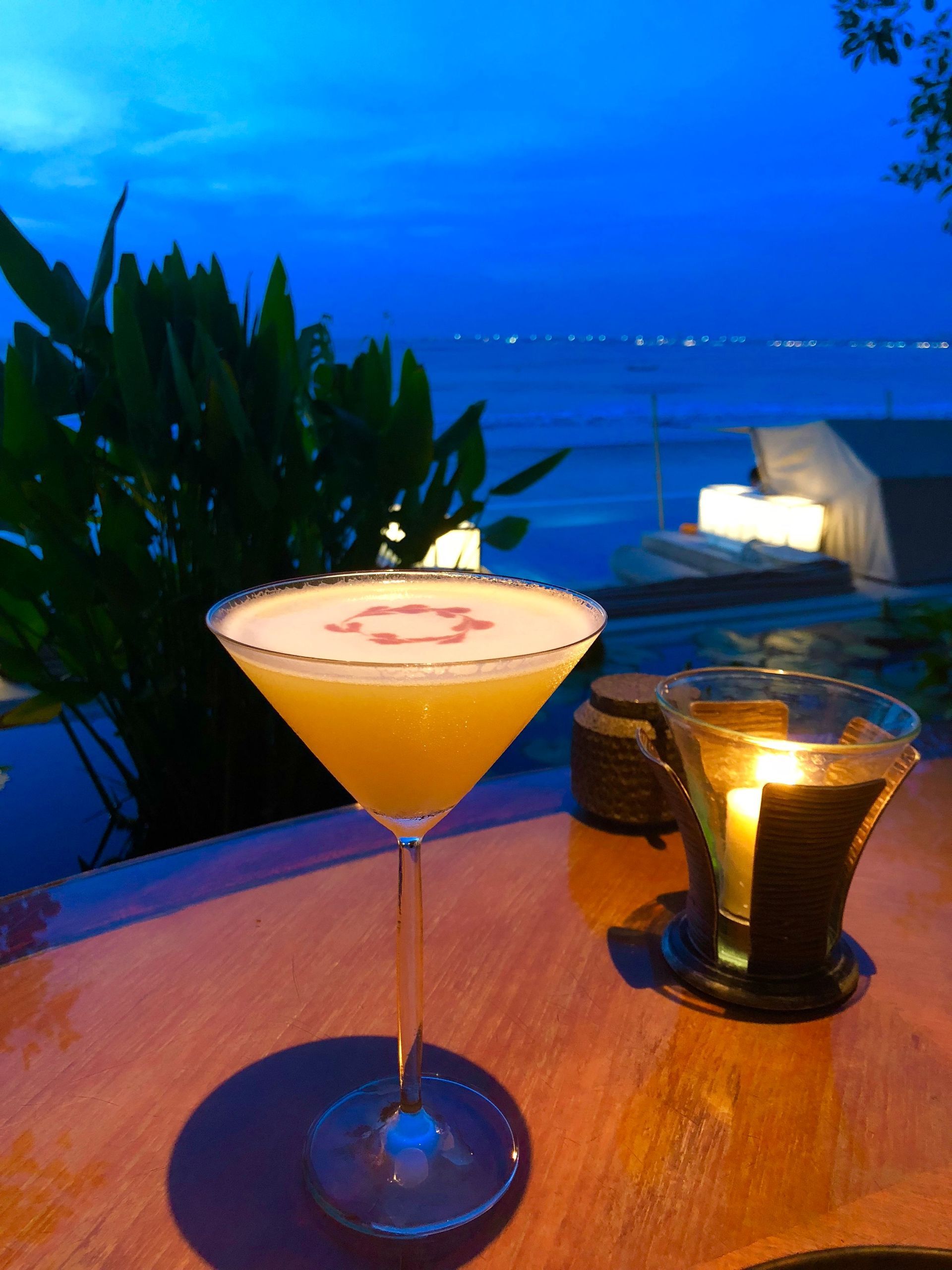 Cocktail on a table at dusk overlooking the ocean, with a glowing candle and lounge seating nearby