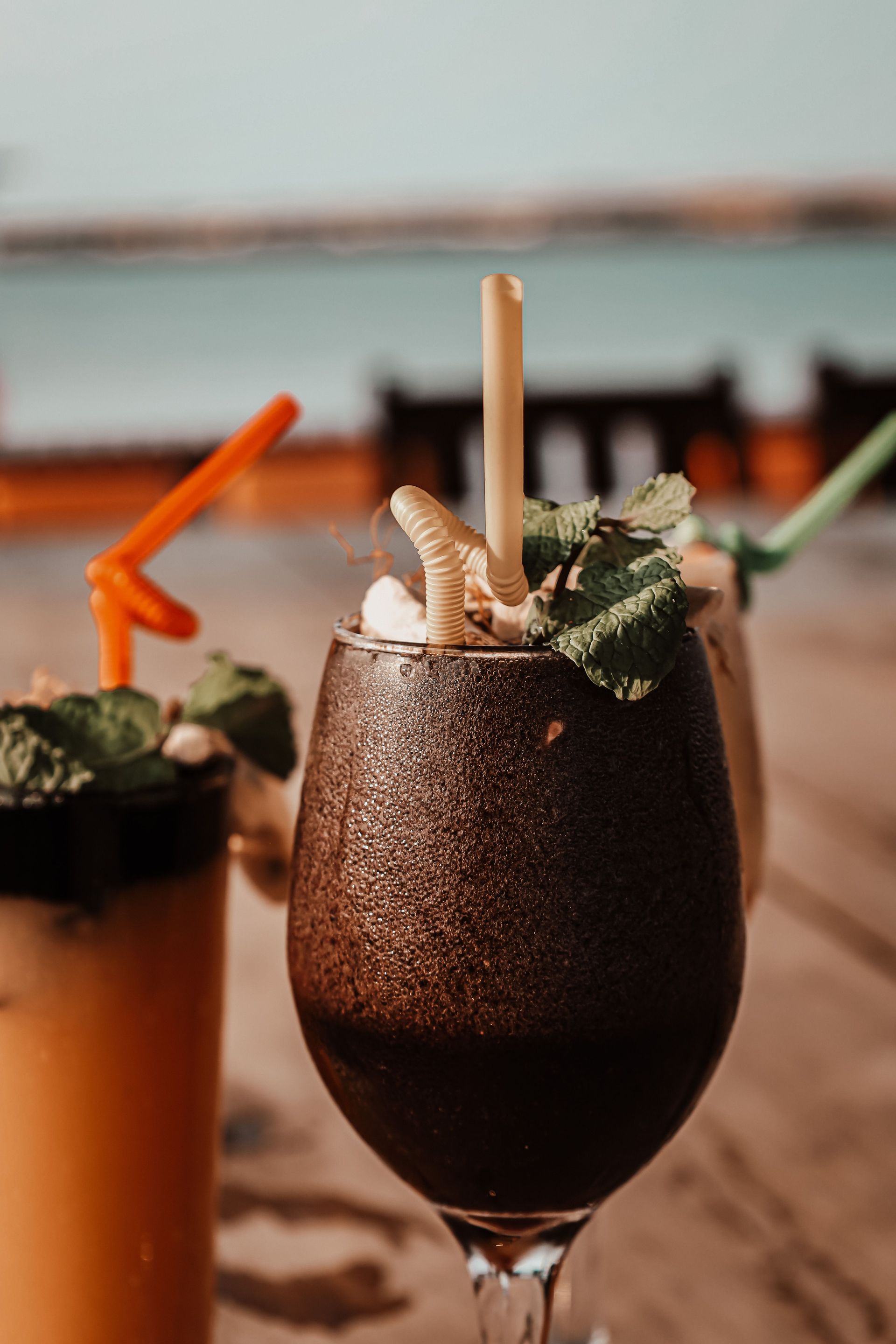 Dark chocolate cocktail in a stemmed glass with straw and mint, on a wooden table by the beach