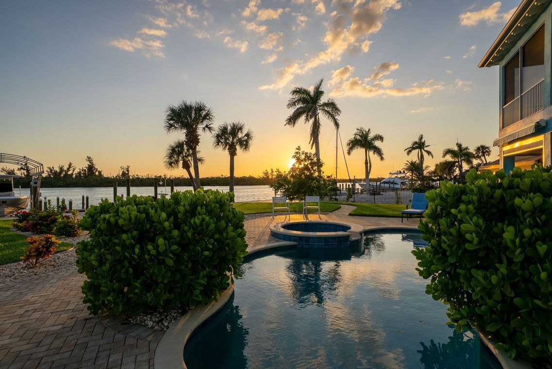 Sunset over a resort pool with palm trees, reflecting water, and ocean in the background