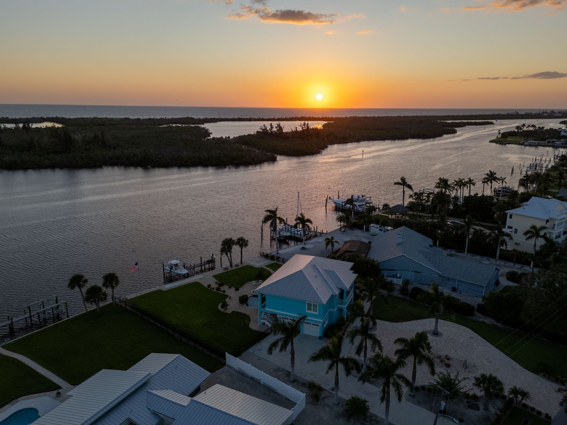 Sunset over a river with waterfront homes, palm trees, and a dock in the foreground