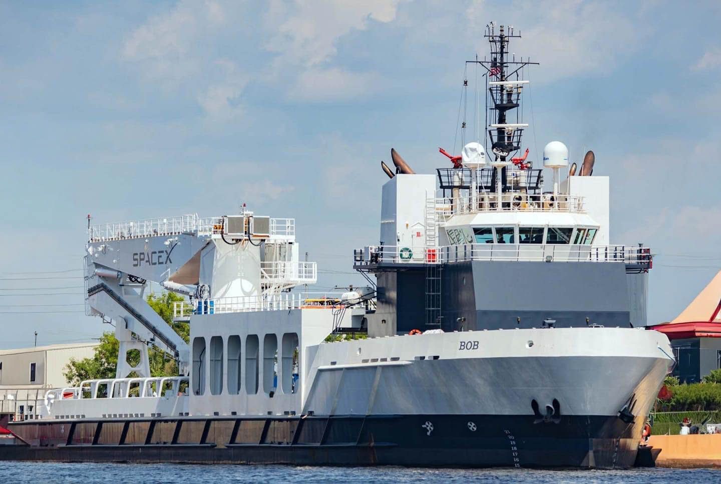 Large white-and-gray research vessel docked by a waterfront, with a crane and radar mast visible.