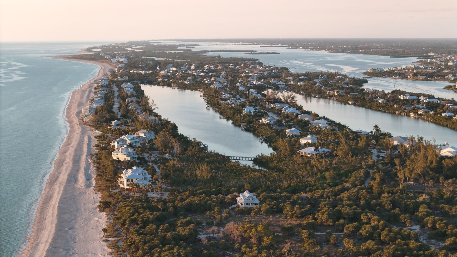 Aerial view of a coastal barrier island with beaches, lagoons, and homes at sunset