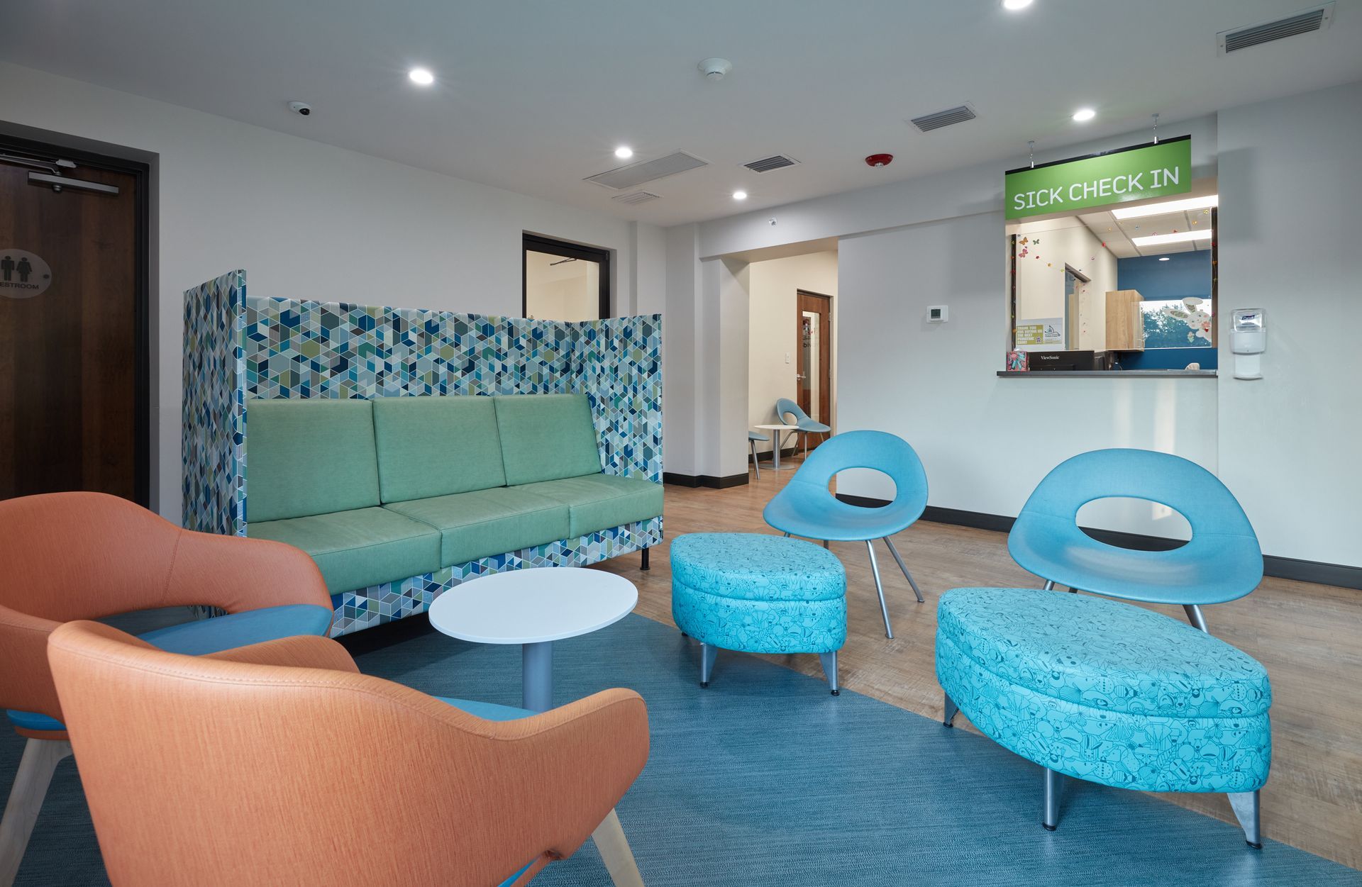 A waiting room with a couch , chairs , ottomans and a table.