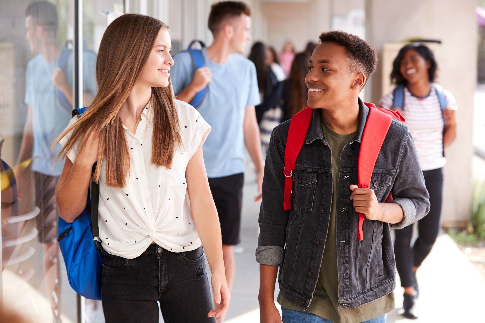 Teenagers walking down a school hallway with backpacks on their backs.