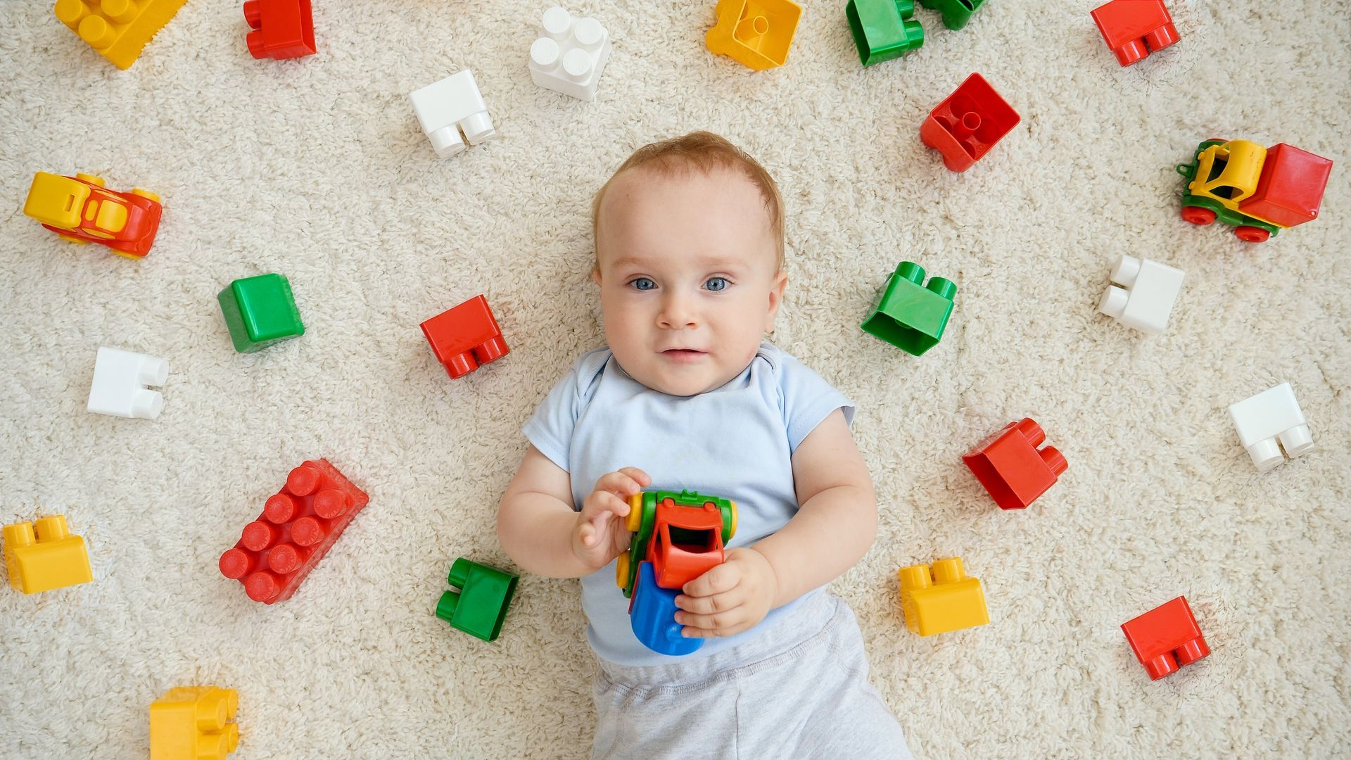 Baby lying on a rug with block toys.