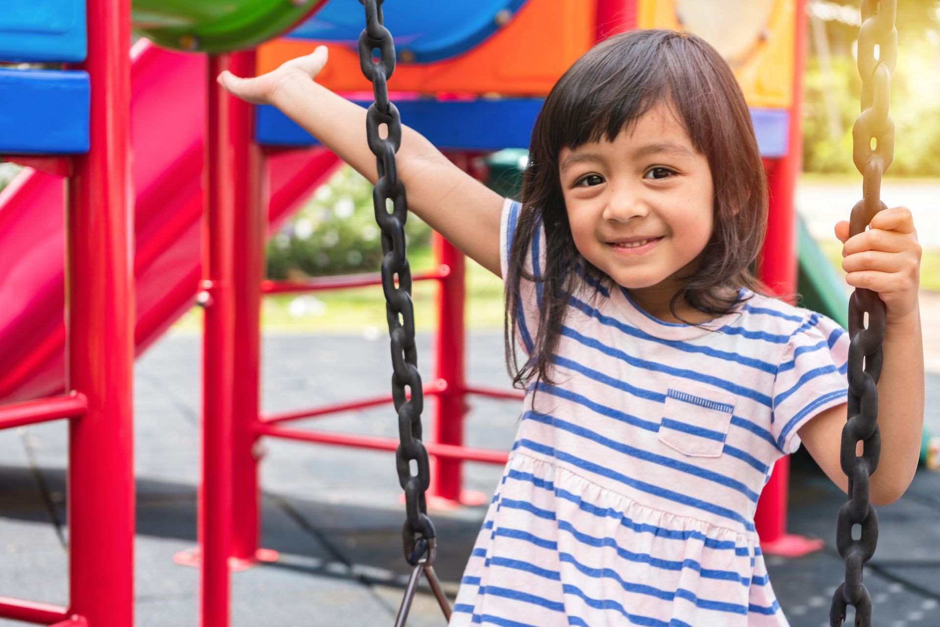 A little girl is sitting on a swing at a playground.