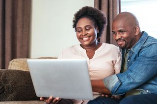 A man and a woman are sitting on a couch looking at a laptop computer.