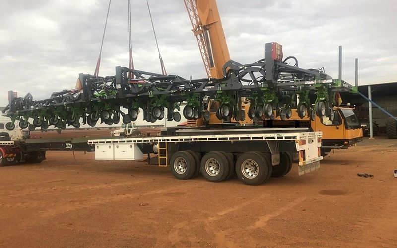 A large agricultural planter being lifted from a flatbed truck by a crane.