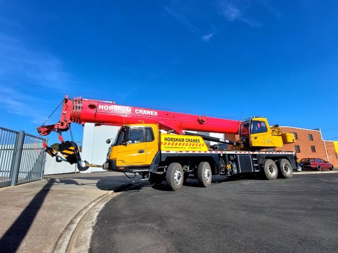 Yellow and red mobile crane on a paved surface, likely at a construction site, under a blue sky.