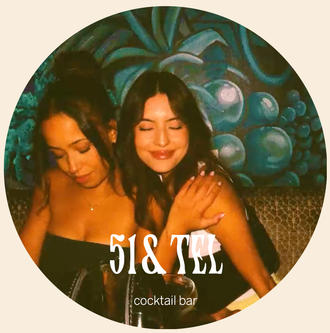 Two women posing closely in front of a teal mural, with “51& TEI” text overlaid near the bottom.
