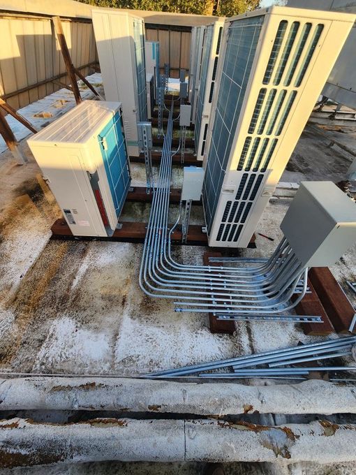 Rooftop HVAC and electrical equipment with metal conduit lines and white units beside a building wall
