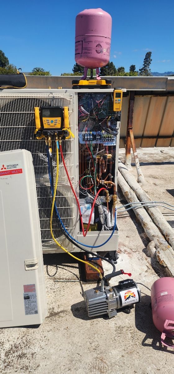 Open electrical control cabinet at an outdoor utility site with pink tanks and pipes nearby.