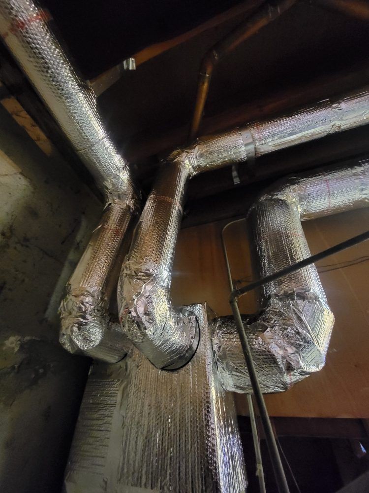 Foil-wrapped HVAC ducts and pipes in a dim mechanical room.