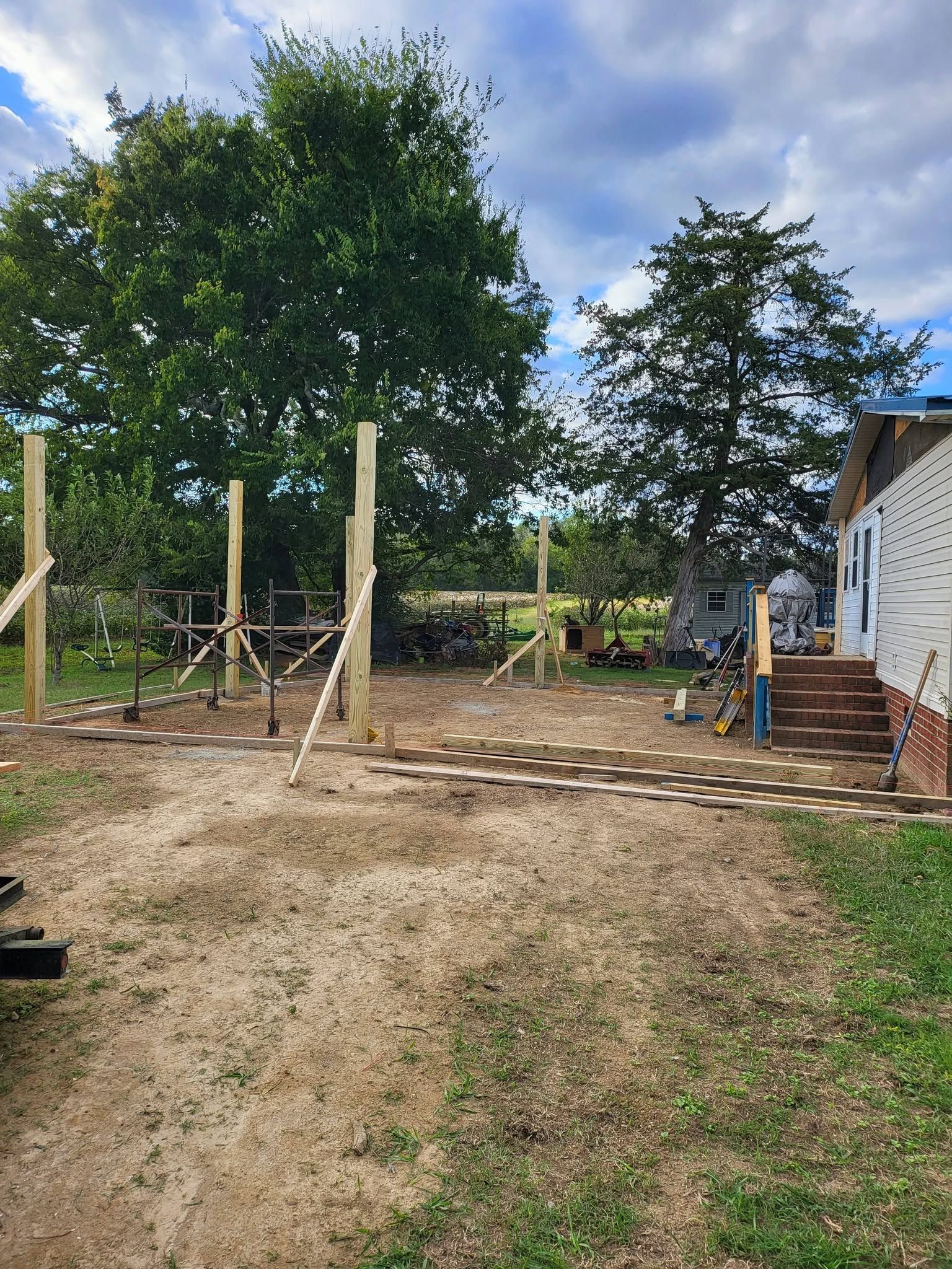 Gravel yard with wooden posts, large trees, and a white house on the right.