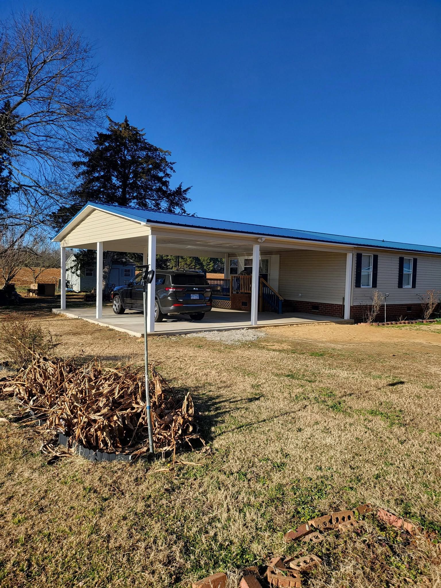 Single-story house with a carport, white siding, and a clear blue sky on a sunny day
