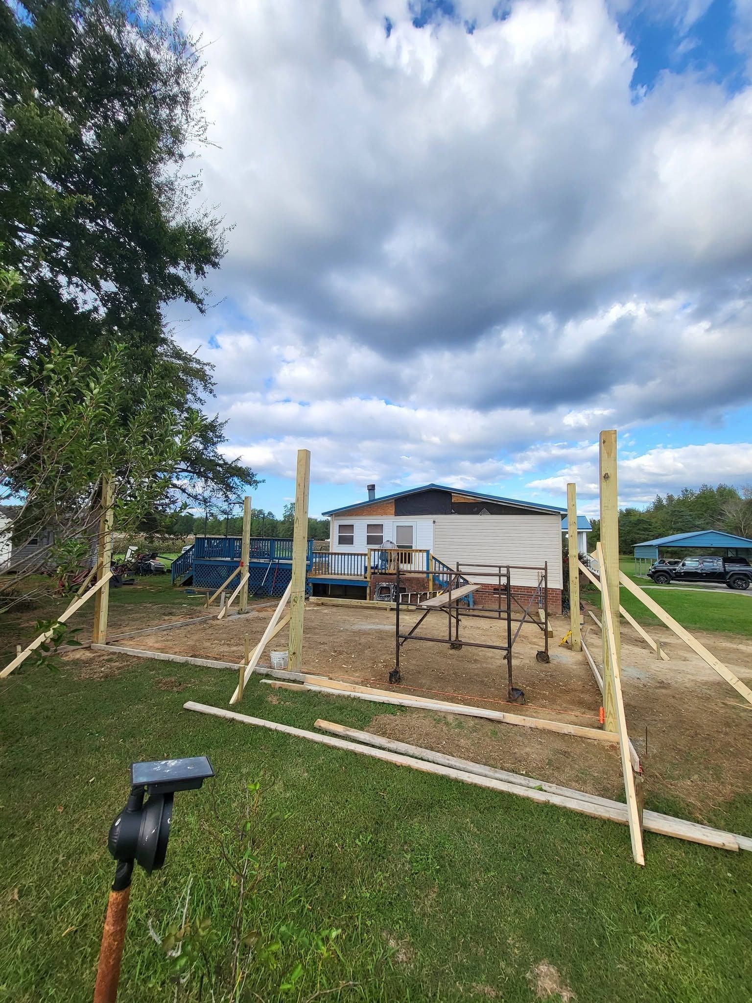 Outdoor construction area with wooden posts and fencing beside a building under a cloudy sky