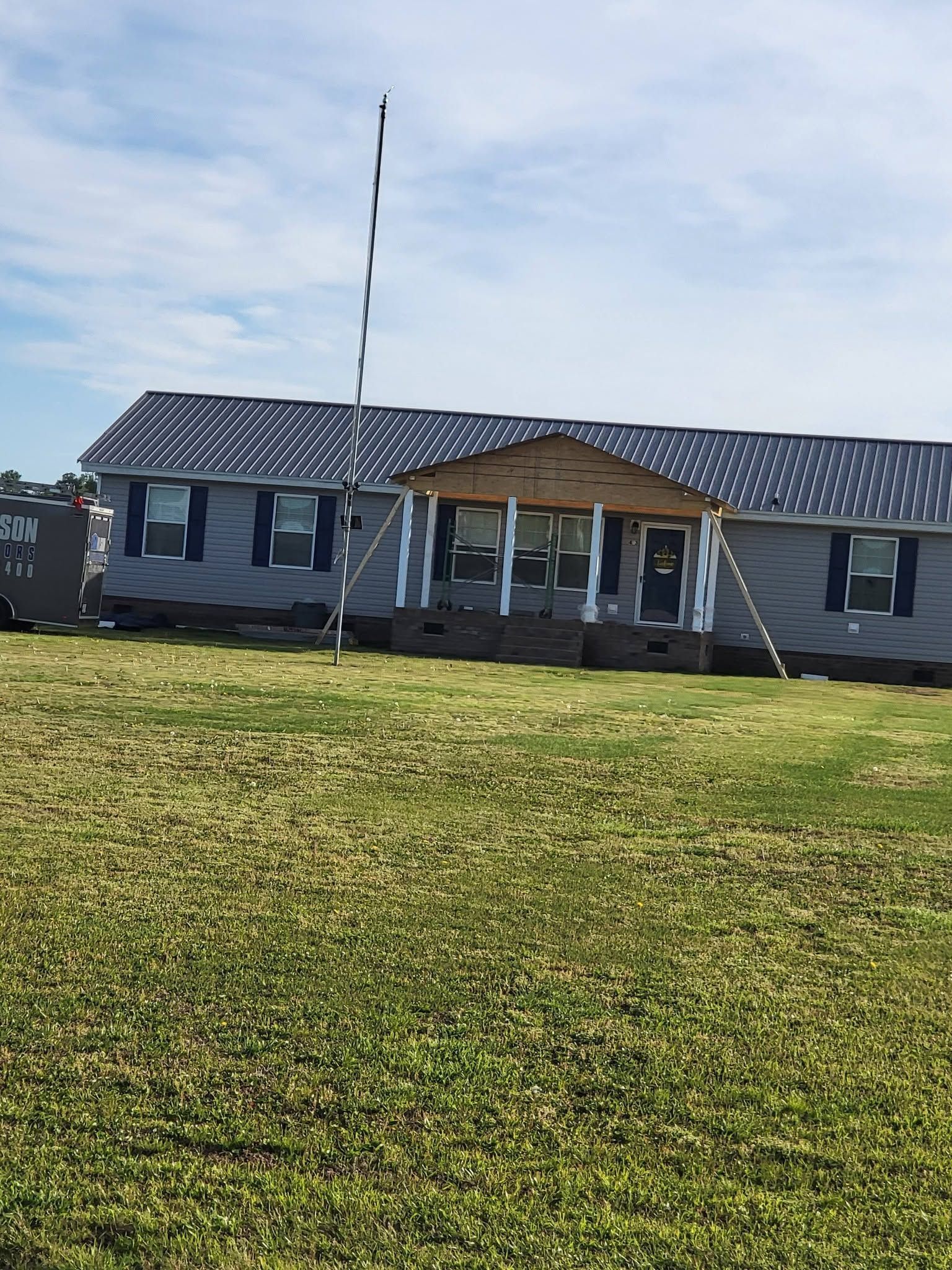 Single-story gray building with a striped metal roof and flagpole, set behind a grassy field.