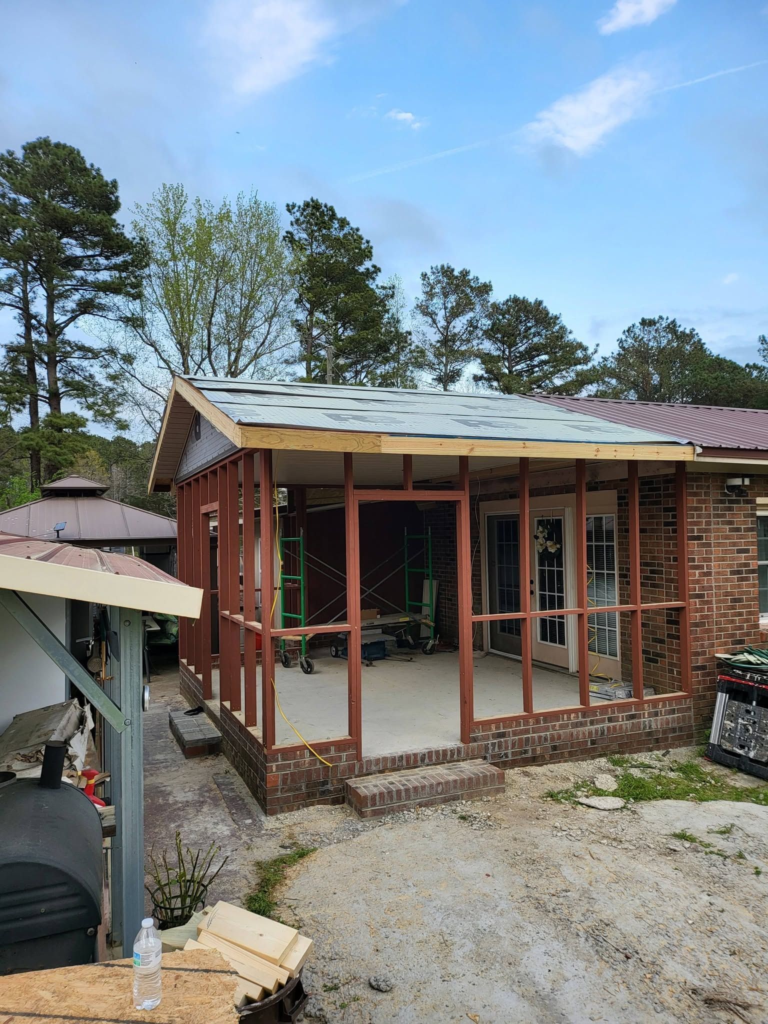 Partially built red wooden shed with large windows and a metal roof in a gravel yard