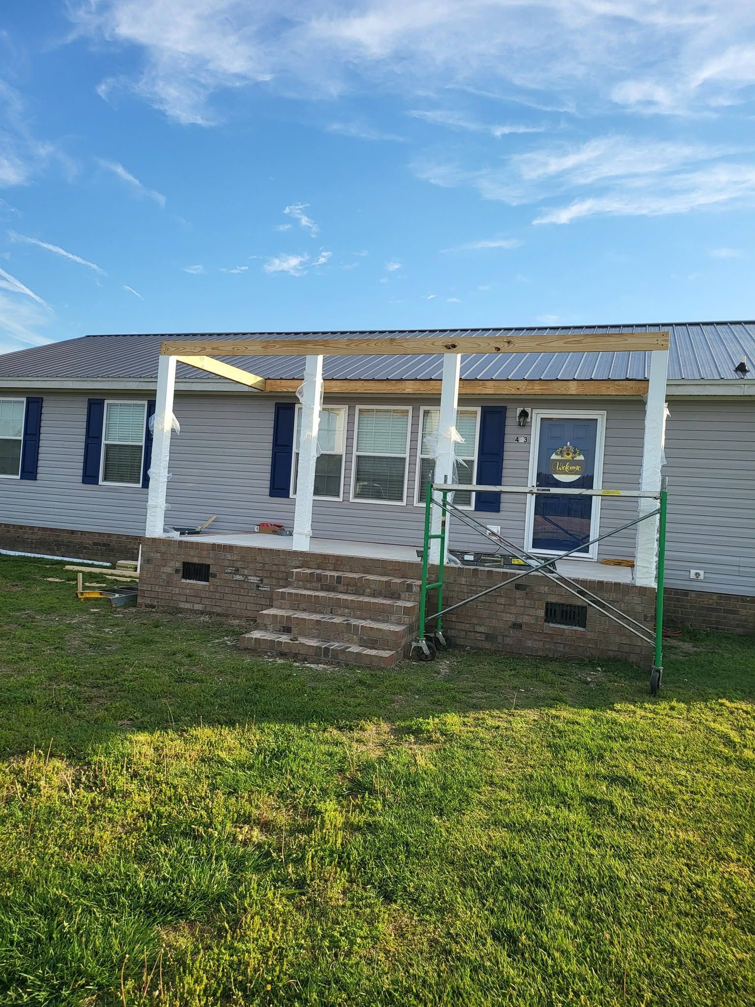 Single-story house with white columns, brick base, and green lawn under a blue sky.