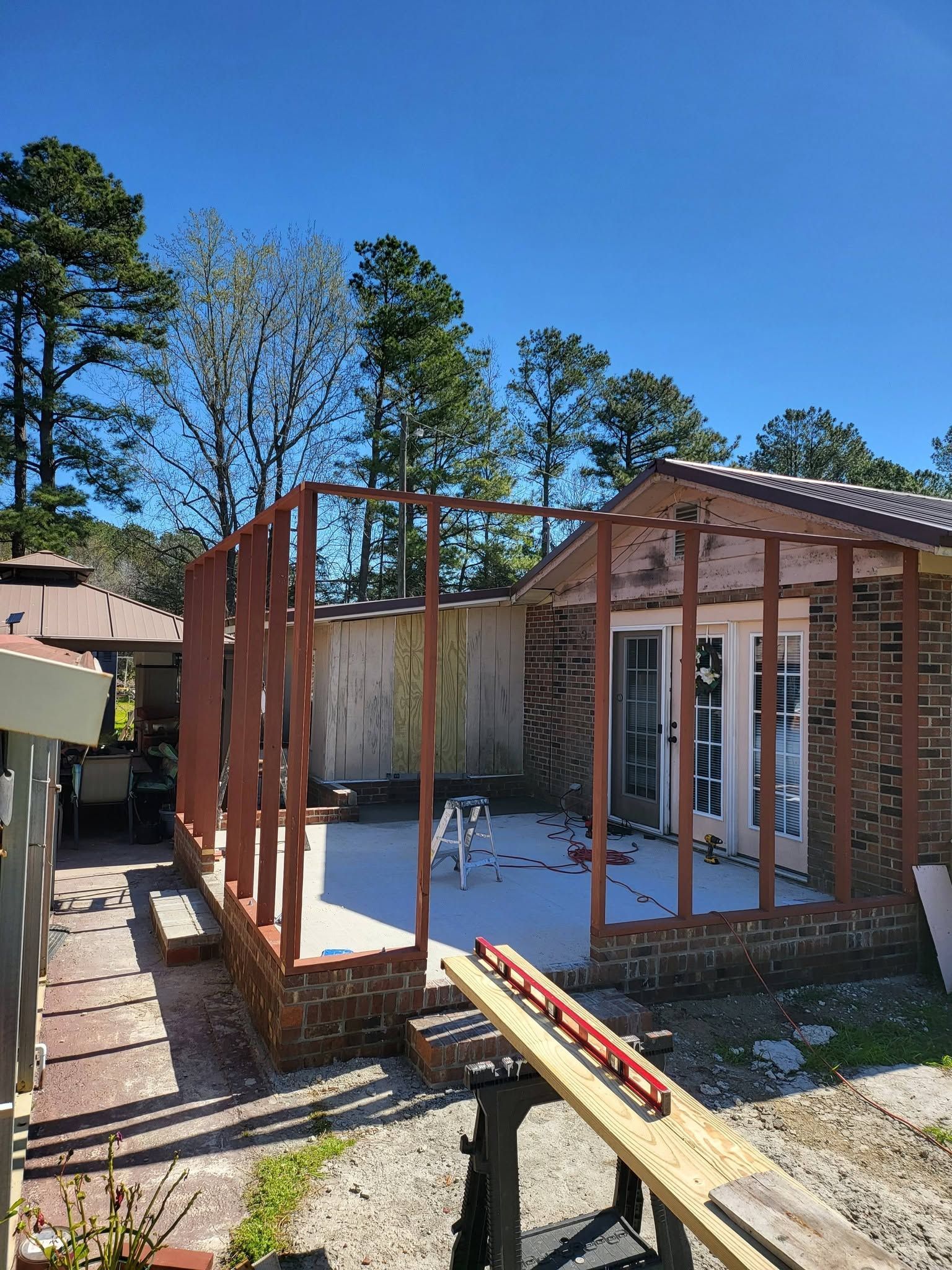 Partially built wooden house frame with white floor, blue sky, and tall trees in the background