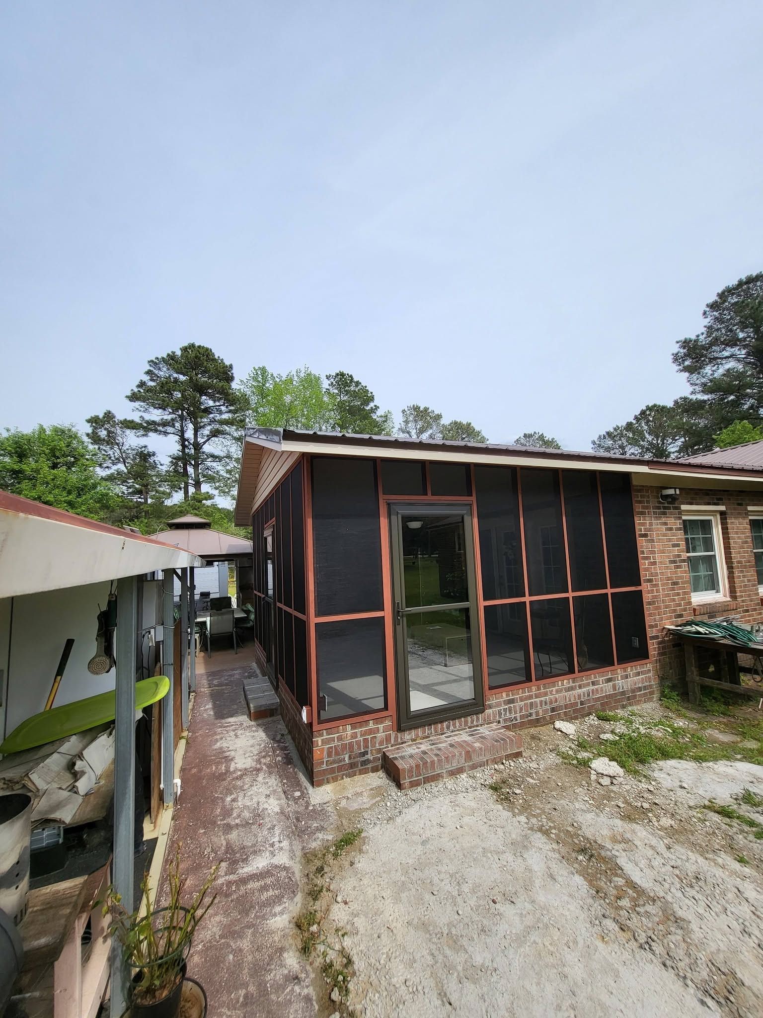 Rural brick house with screened porch and gravel driveway, viewed from the yard on a sunny day