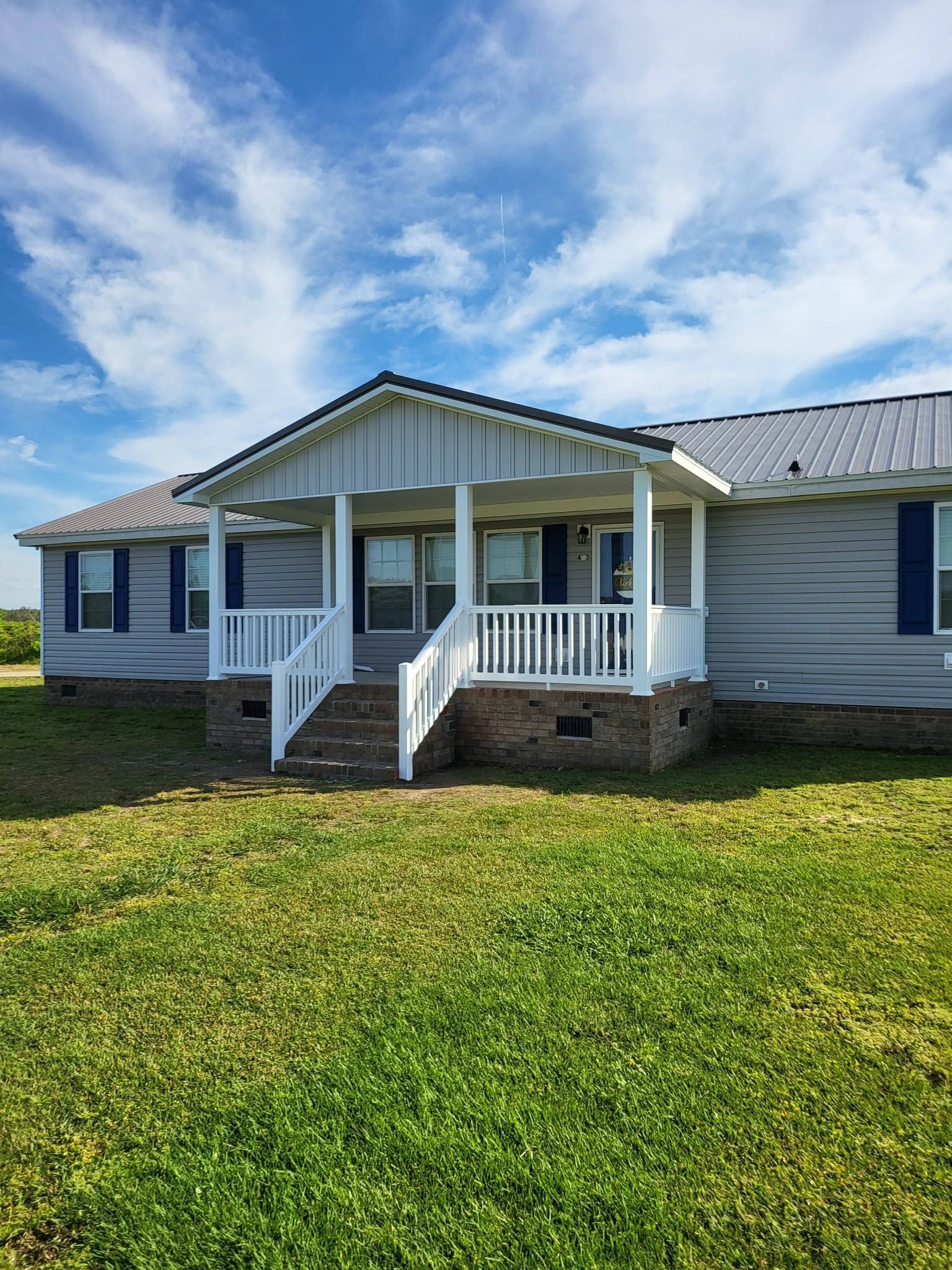 White house with a front porch and steps under a blue sky, surrounded by a grassy yard