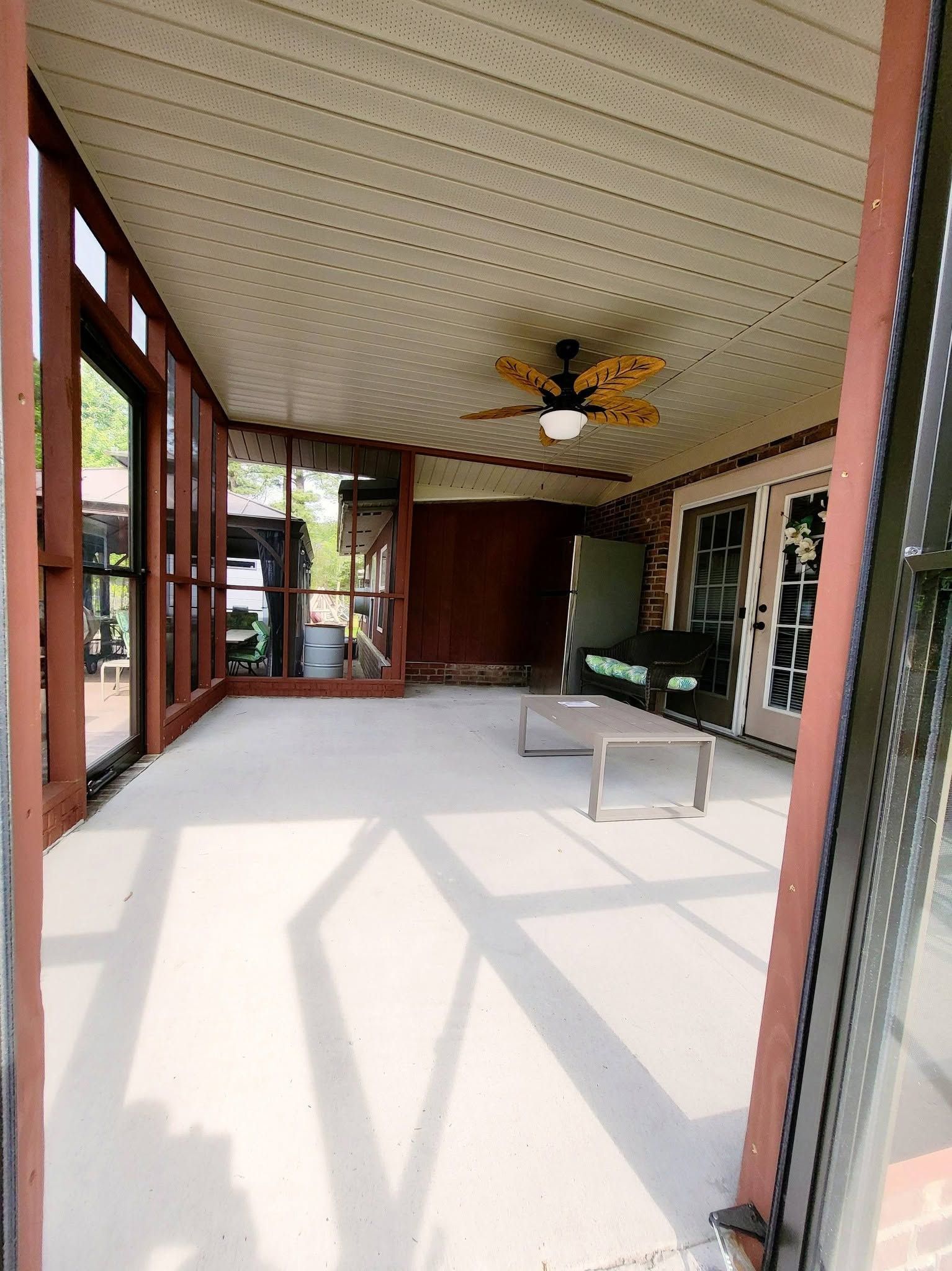Sunroom with white ceiling, ceiling fan, glass walls, and a small table on a tiled floor.