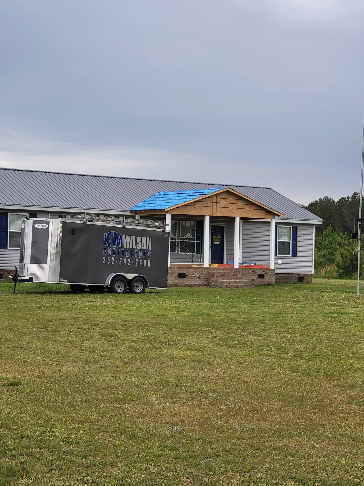 Mobile trailer parked on grass in front of a small white house with a partially damaged roof.