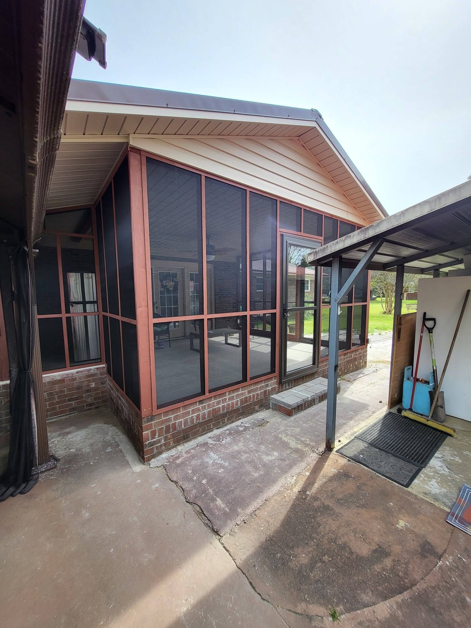 Exterior of a house with large screened windows, a covered walkway, and a concrete patio.
