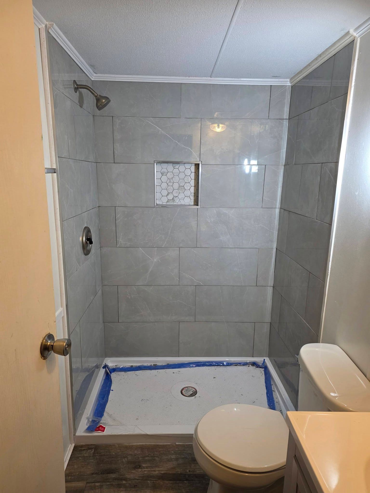 Small tiled bathroom with a shower, toilet, and sink under renovation, with blue tape around the shower base.