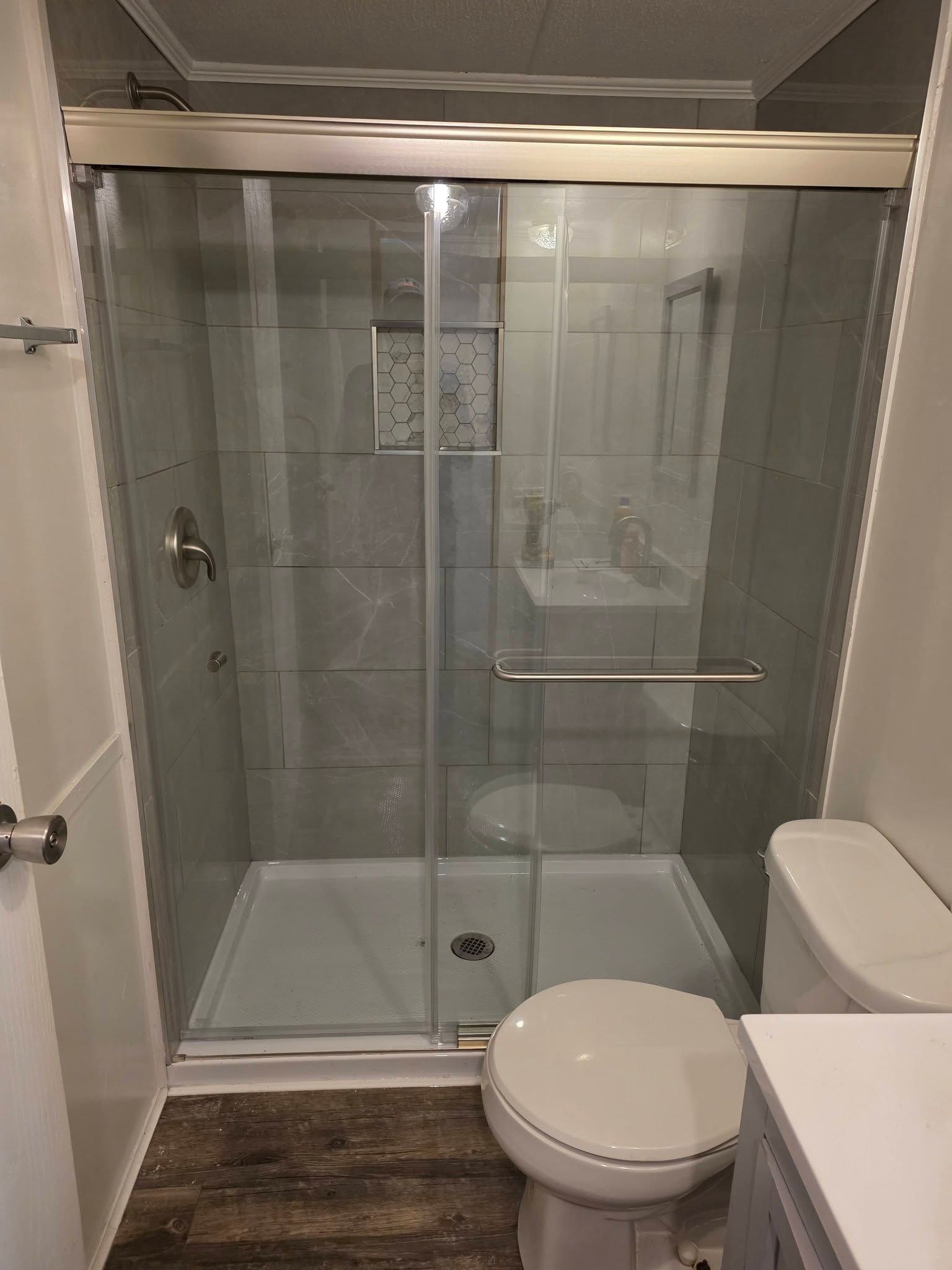 Small bathroom with a glass shower stall, white toilet, and brown wood-pattern floor.