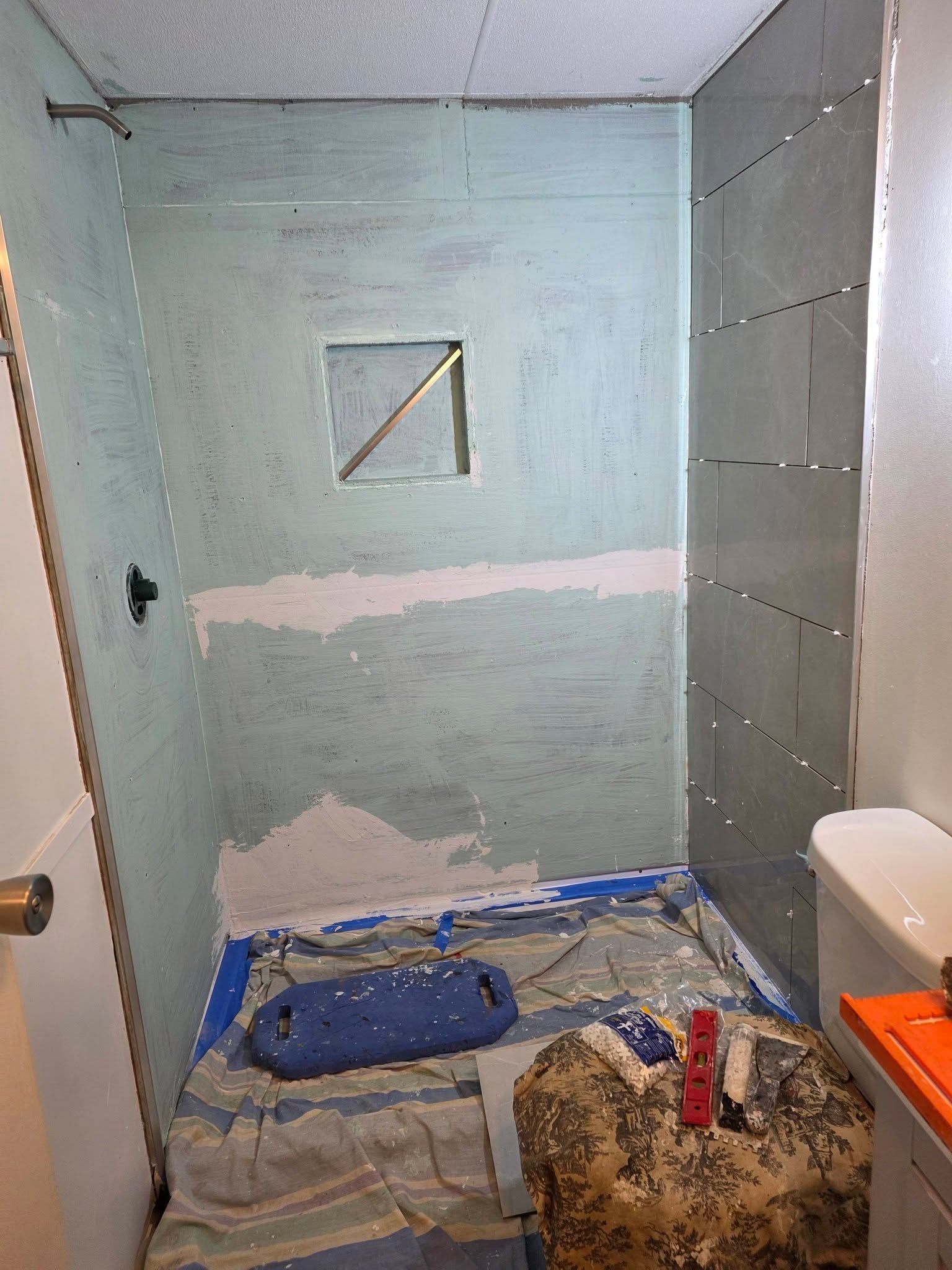 Bathroom renovation with pale blue walls, unfinished drywall, and tools and drop cloths on the floor