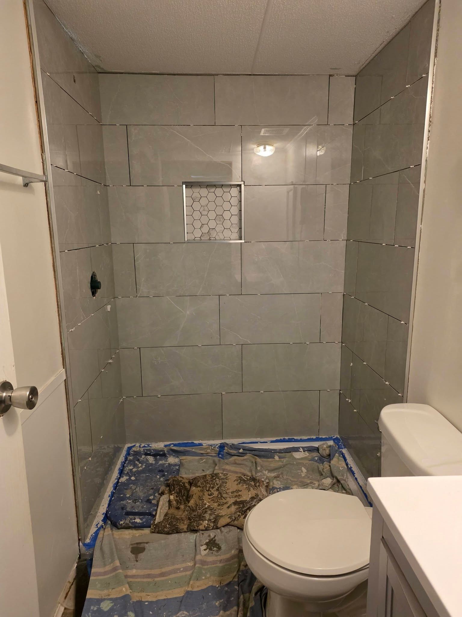Damaged bathroom under repair with exposed floor, tiled walls, toilet, and vanity in view