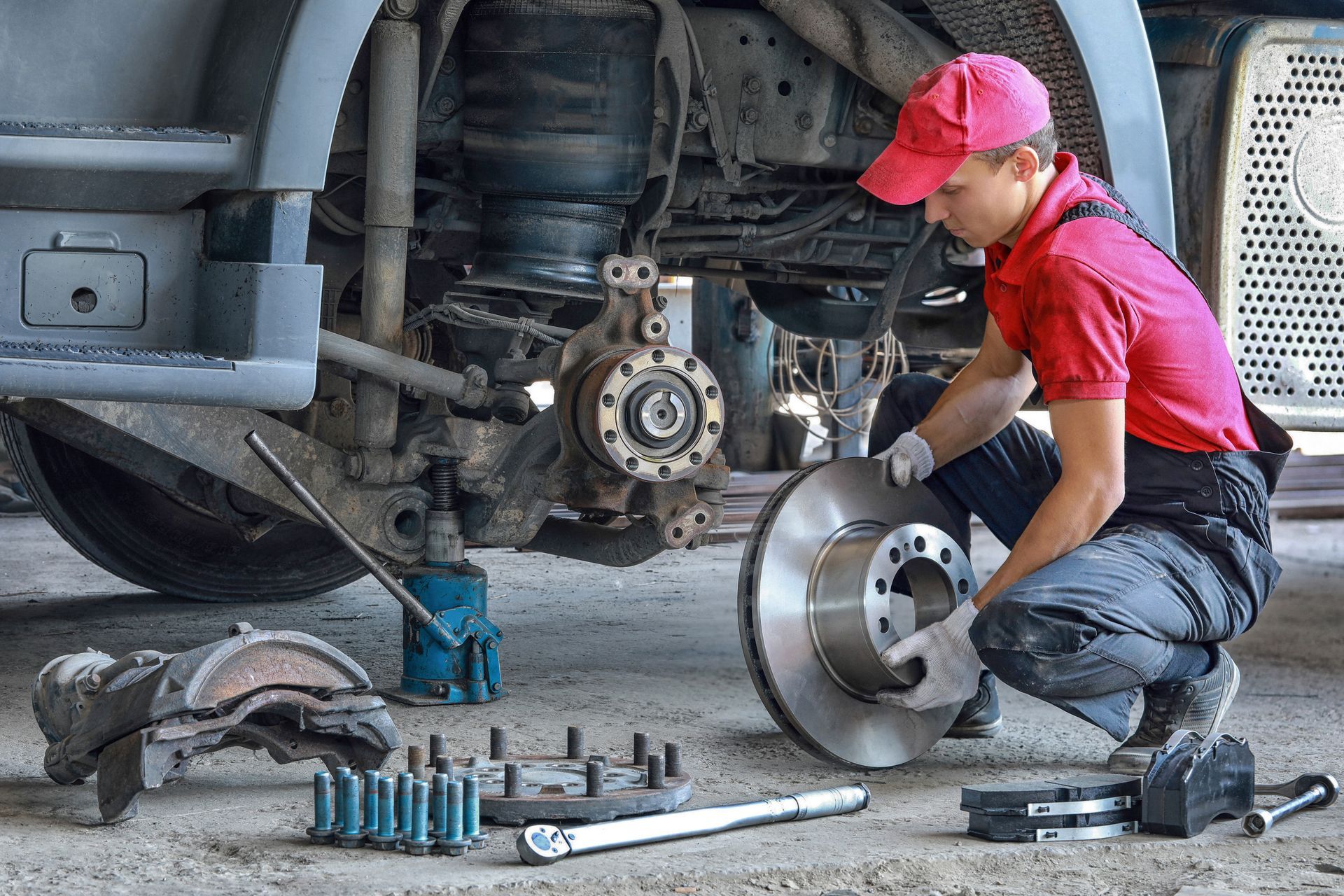 A mechanic next to the trailer, with spare parts, repairs a truck, replacing a brake disc and pads.