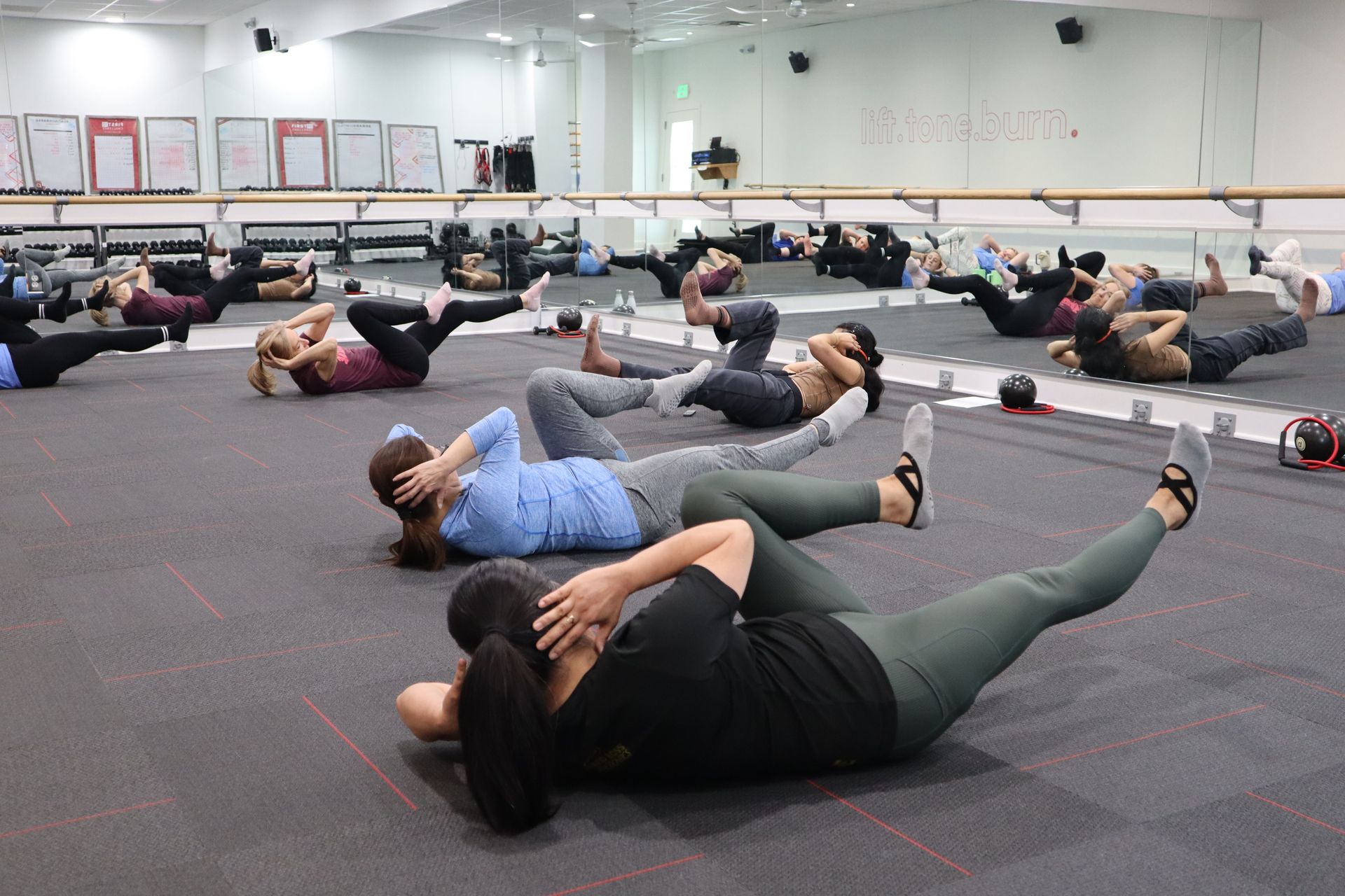 Un athlète se tient debout sur des ballons médicinaux dans une salle de sport, tandis que d'autres personnes s'entraînent en arrière-plan.