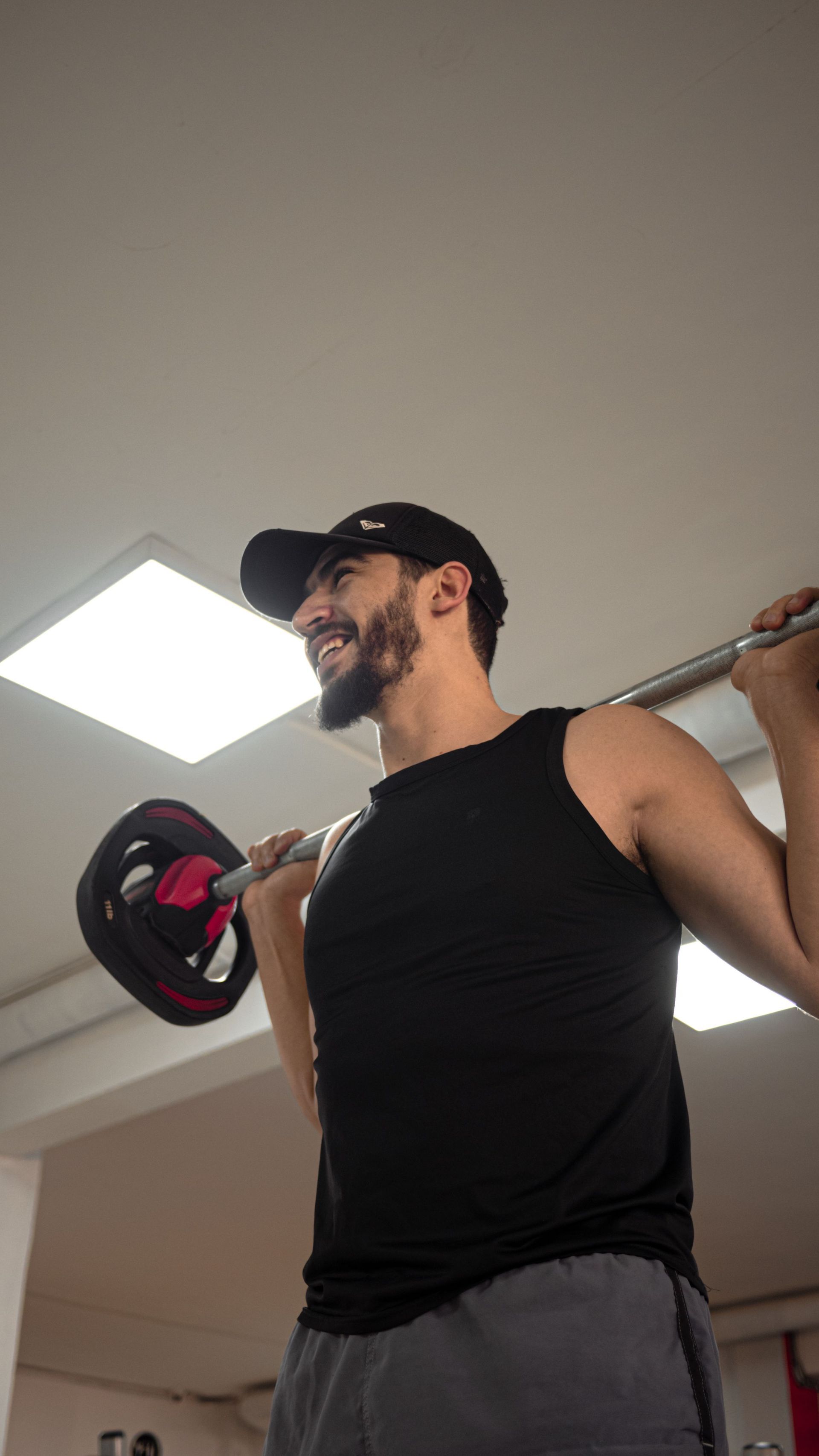 Un athlète se tient debout sur des ballons médicinaux dans une salle de sport, tandis que d'autres personnes s'entraînent en arrière-plan.