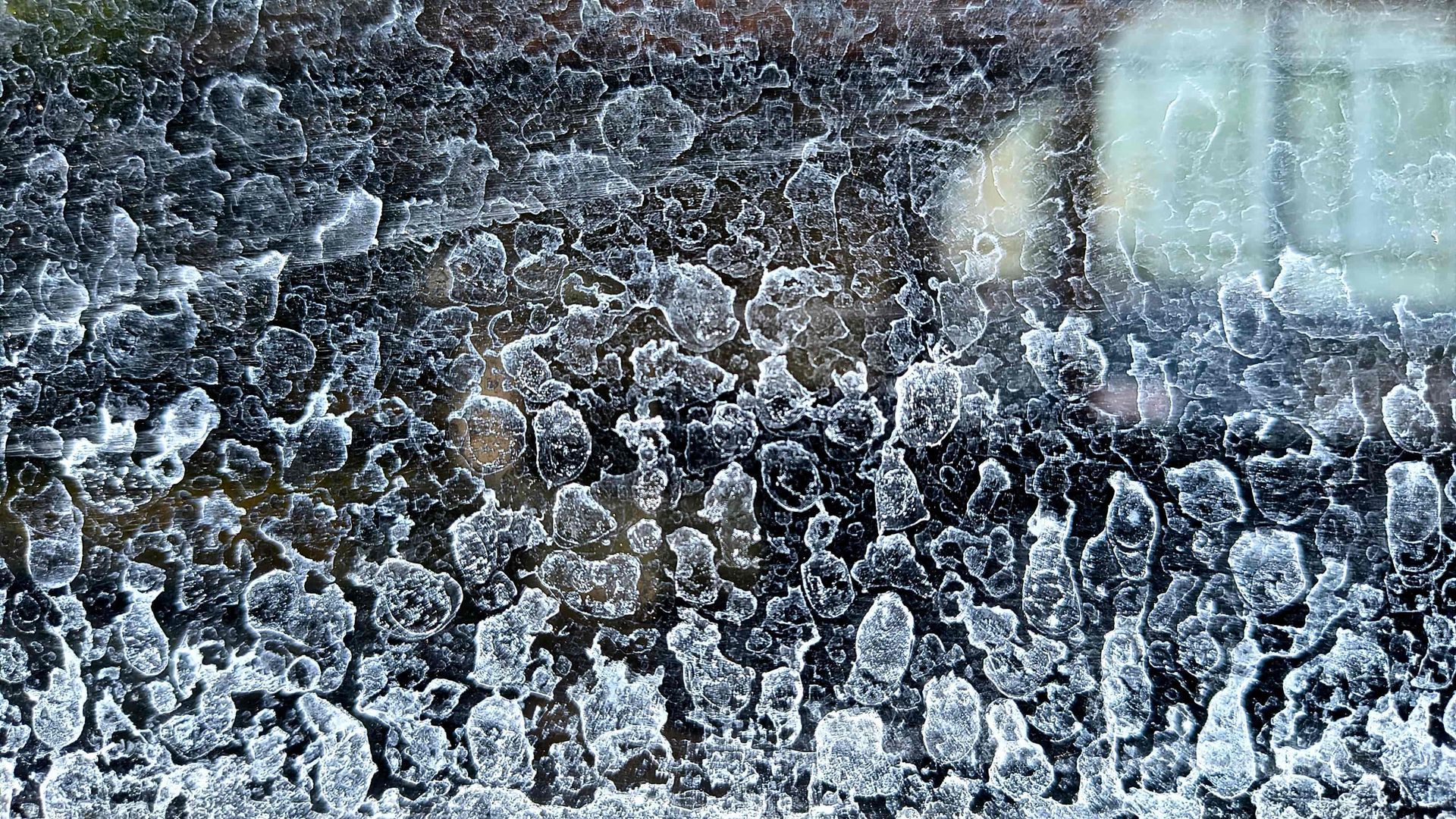 Icy, frost-covered glass with blurred lights reflected in the background.