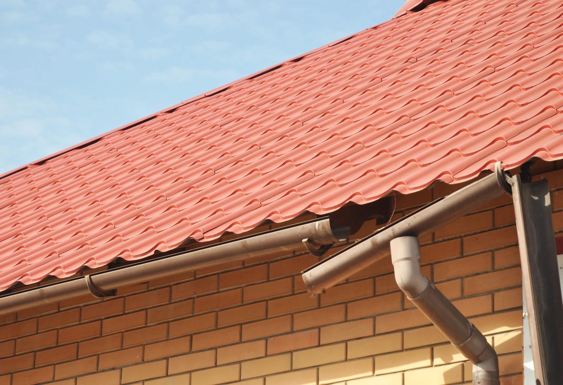 Red tiled roof with brick wall and rain gutter on a house.
