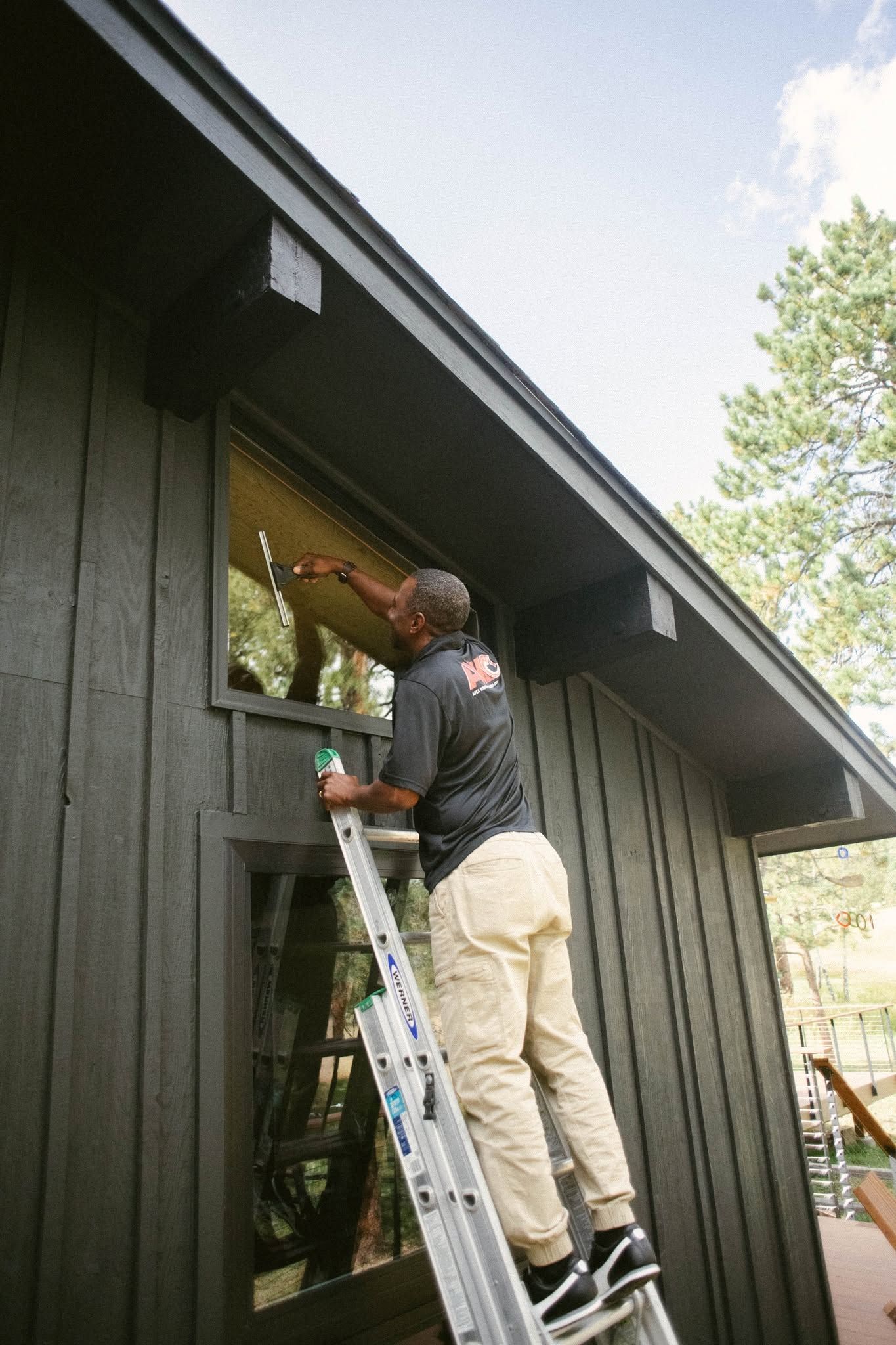 Person on a ladder painting the exterior of a dark house near the roofline.