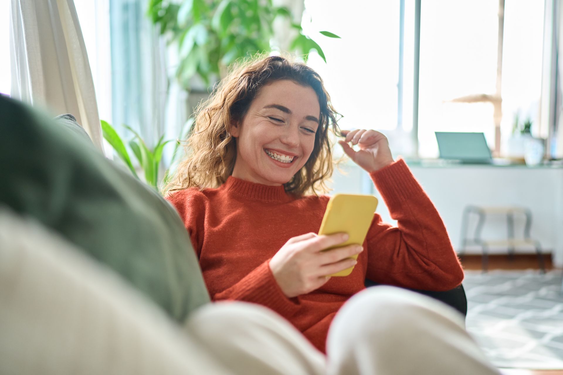Woman smiling on a couch and looking at her phone in a bright living room