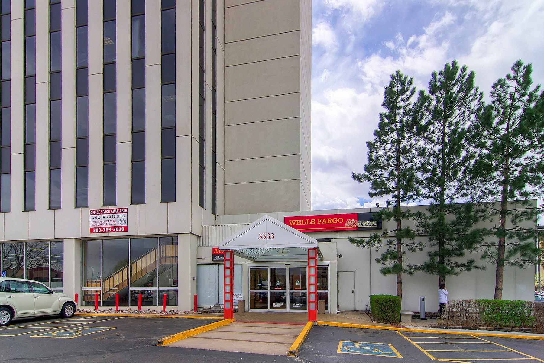 Hospital entrance with red awning, glass doors, parked cars, and tall building facade