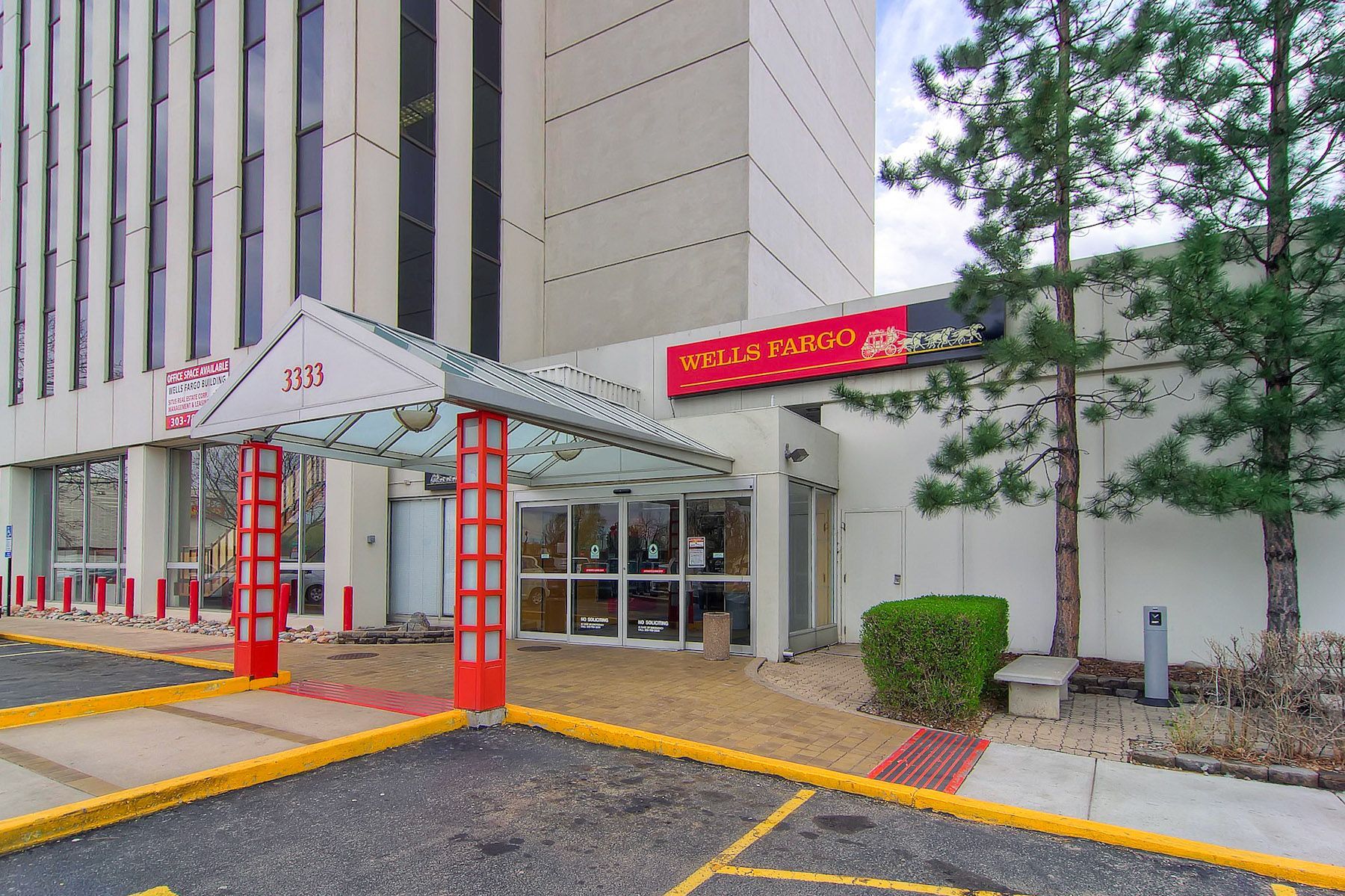Covered hotel entrance with red sign, glass doors, and a paved driveway beside a tall building