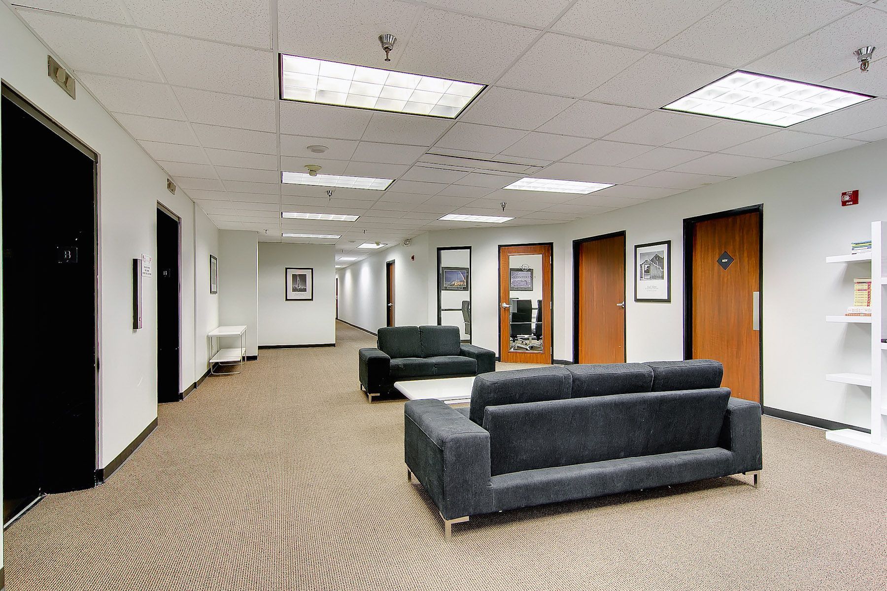 Empty office hallway with carpet, gray couches, doors, and framed wall art