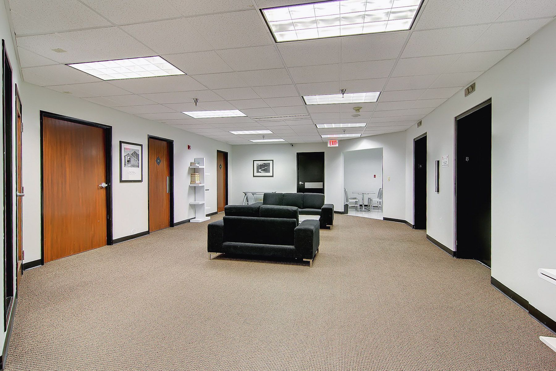 Empty office lobby with black sofas, patterned carpet, and white walls under fluorescent lights