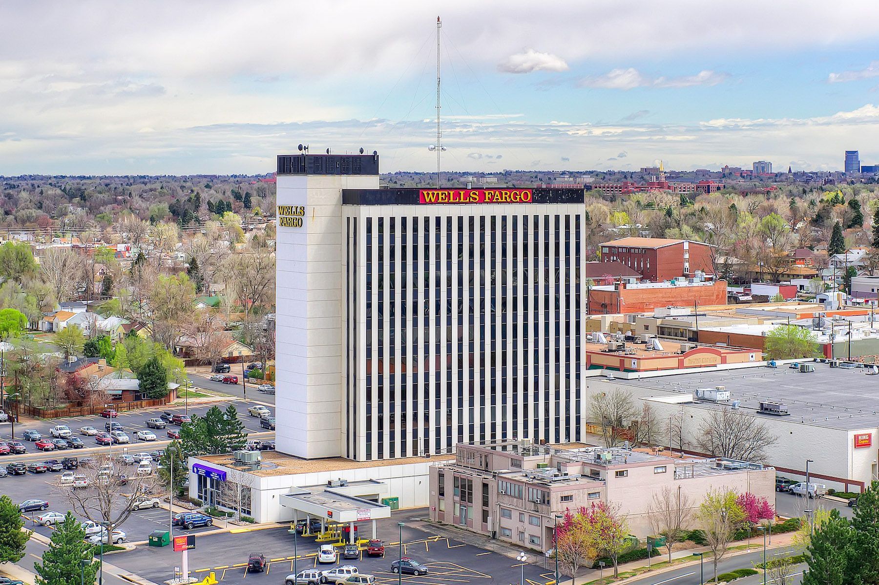 A tall hotel tower rises above a cityscape with trees, roads, and low buildings under a cloudy sky.