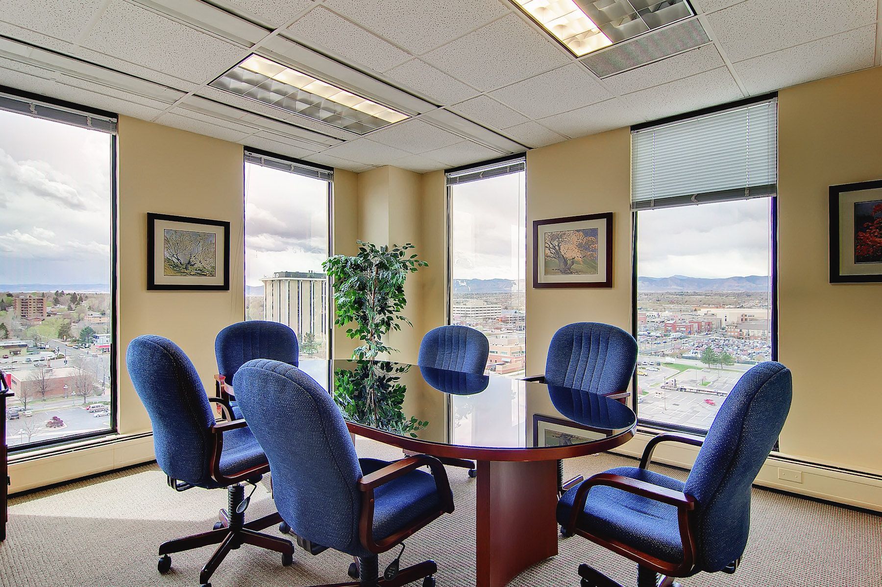 Small office meeting area with blue chairs around a round table by large windows.