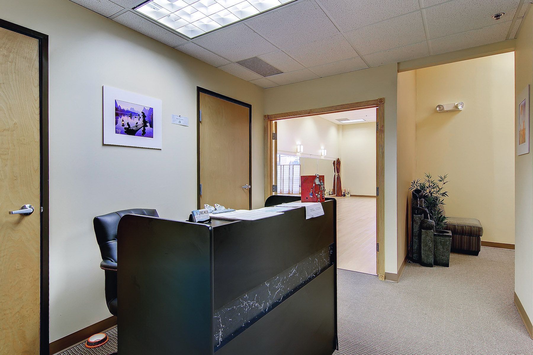 Empty office lobby with a black reception desk, beige walls, and an open doorway to a hallway.