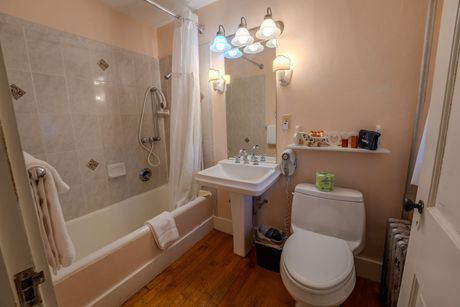 Bathroom with a bathtub, sink, and toilet. Pink walls, wood floor, and a lit mirror.